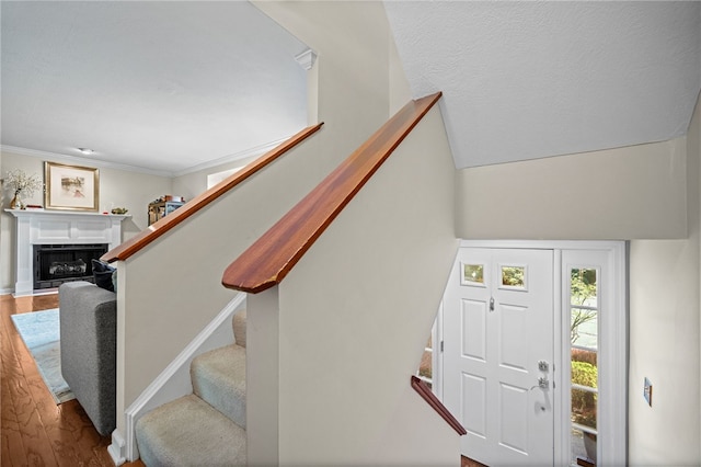 entrance foyer with stairs, wood finished floors, a fireplace, and ornamental molding