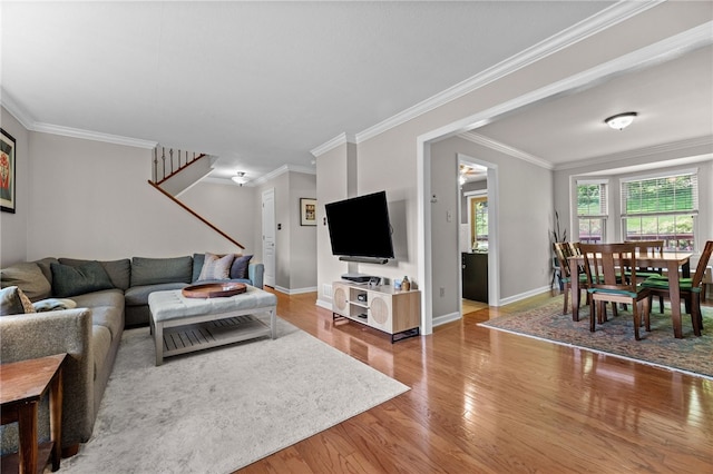 living area featuring stairway, wood finished floors, baseboards, and crown molding