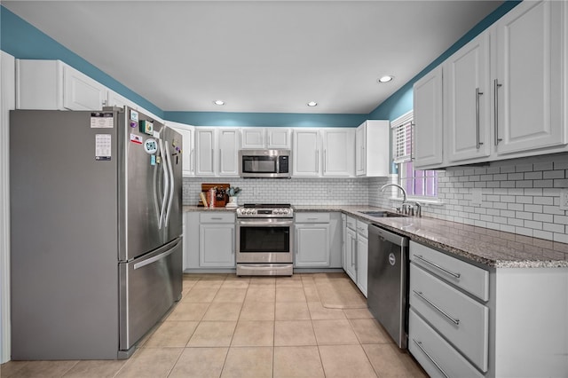 kitchen featuring appliances with stainless steel finishes, a sink, light tile patterned flooring, light stone countertops, and white cabinetry