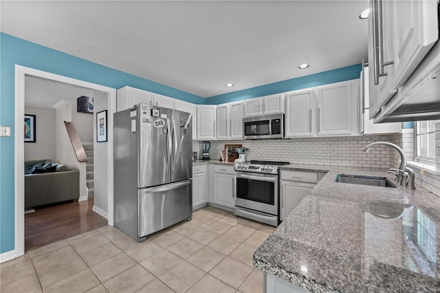 kitchen with stainless steel appliances, a sink, light stone counters, backsplash, and white cabinetry