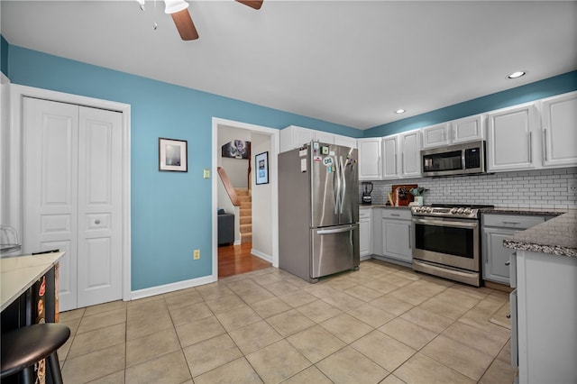kitchen with appliances with stainless steel finishes, ceiling fan, backsplash, light tile patterned floors, and white cabinets