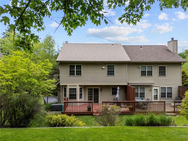 rear view of property featuring a chimney, a yard, a deck, and roof with shingles