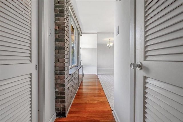 corridor featuring brick wall, wood finished floors, a chandelier, and baseboards