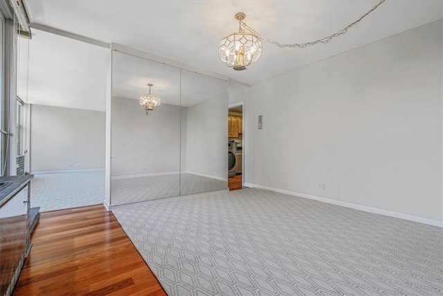 unfurnished room with a chandelier, wood finished floors, washer / dryer, and baseboards