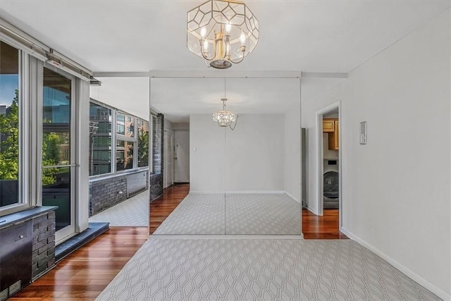 unfurnished dining area featuring a chandelier, wood finished floors, baseboards, and washer / dryer