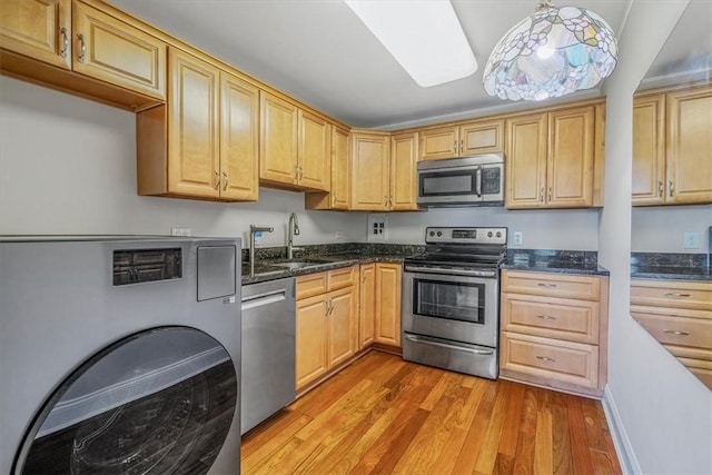 kitchen featuring appliances with stainless steel finishes, light wood-style floors, a sink, washer / clothes dryer, and dark stone countertops