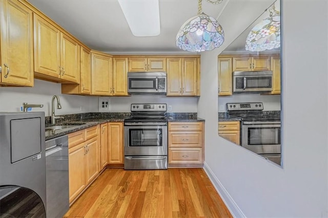 kitchen featuring appliances with stainless steel finishes, a sink, light wood-style flooring, dark stone countertops, and light brown cabinets