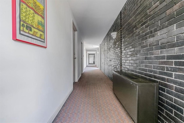hall featuring baseboards, carpet, and brick wall