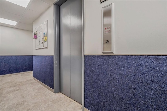 hall featuring a wainscoted wall, a drop ceiling, and elevator