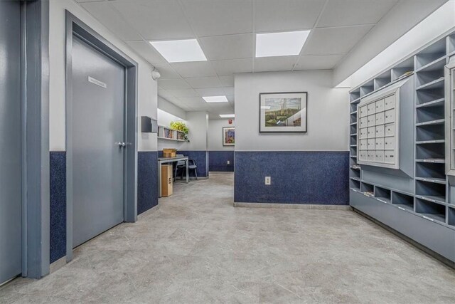 view of home's community with a paneled ceiling, mail area, and a wainscoted wall