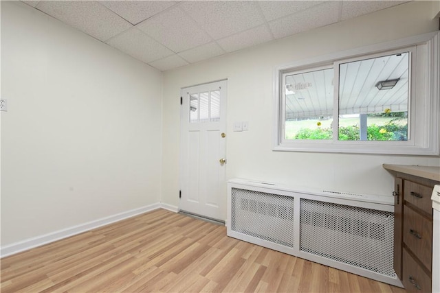 unfurnished room featuring radiator heating unit, light wood-type flooring, baseboards, and a paneled ceiling