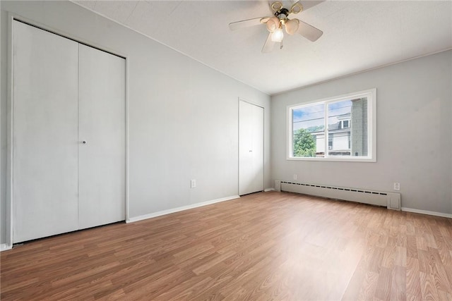 unfurnished bedroom with a baseboard heating unit, light wood-style floors, two closets, and baseboards