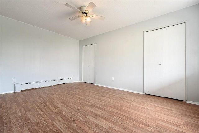 unfurnished bedroom with a baseboard heating unit, multiple closets, wood finished floors, baseboards, and a ceiling fan