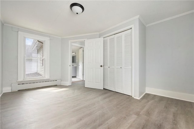 unfurnished bedroom with a baseboard heating unit, crown molding, wood finished floors, baseboards, and a closet