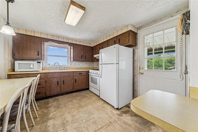 kitchen featuring white appliances, a sink, a textured ceiling, light countertops, and hanging light fixtures