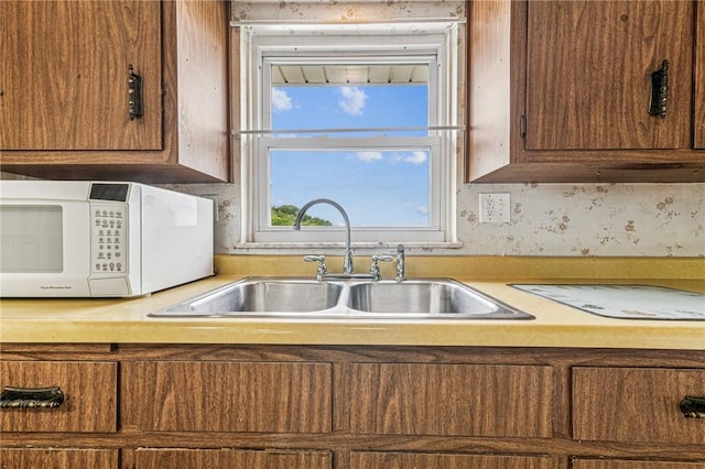 kitchen featuring white microwave, a sink, light countertops, and brown cabinetry
