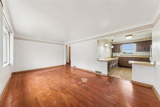 unfurnished living room with a sink, light wood-style flooring, baseboards, and ornamental molding
