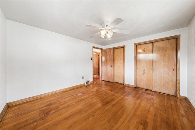 unfurnished bedroom with multiple closets, wood finished floors, a ceiling fan, and baseboards