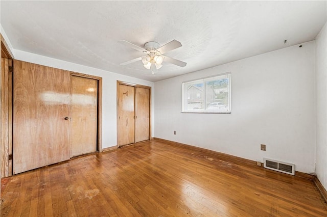unfurnished bedroom featuring two closets, hardwood / wood-style floors, baseboards, and ceiling fan