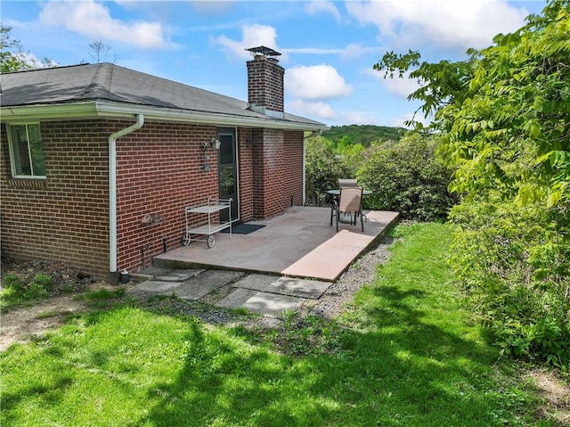 rear view of property with a patio area, a chimney, brick siding, and a yard