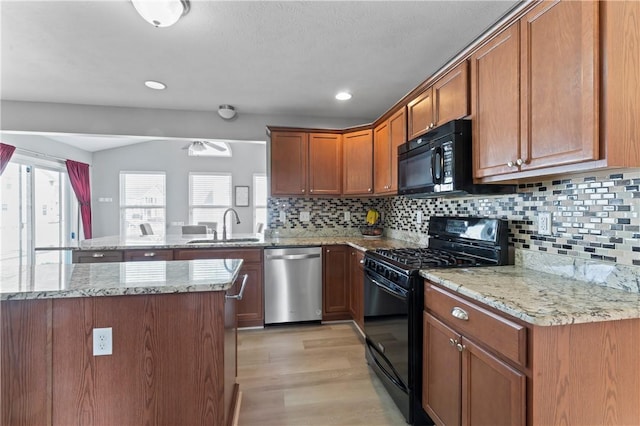kitchen with black appliances, a sink, a peninsula, light wood finished floors, and brown cabinetry
