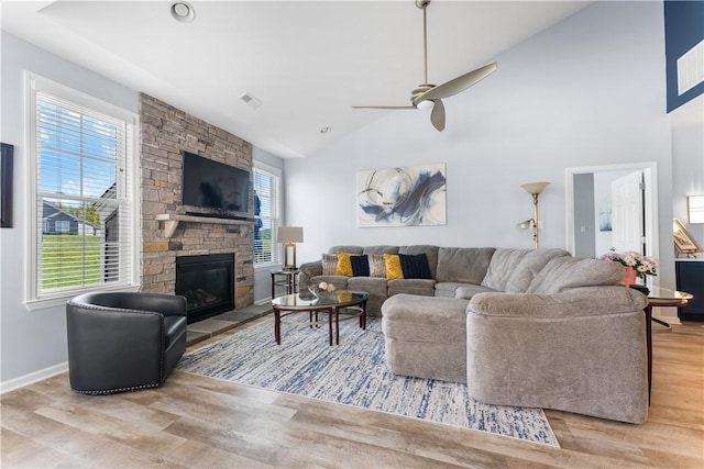 living area with wood finished floors, ceiling fan, high vaulted ceiling, a stone fireplace, and baseboards