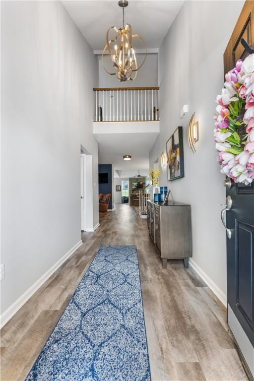 entryway featuring a towering ceiling, a chandelier, wood finished floors, and baseboards