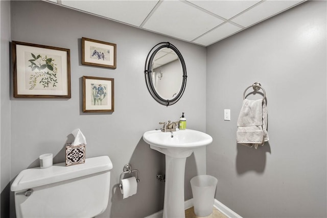half bath featuring toilet, a drop ceiling, a sink, and baseboards