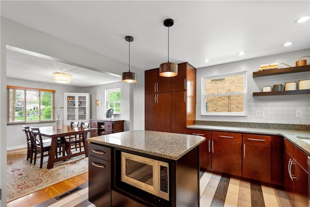 kitchen with stainless steel microwave, light wood finished floors, open shelves, decorative light fixtures, and light stone counters