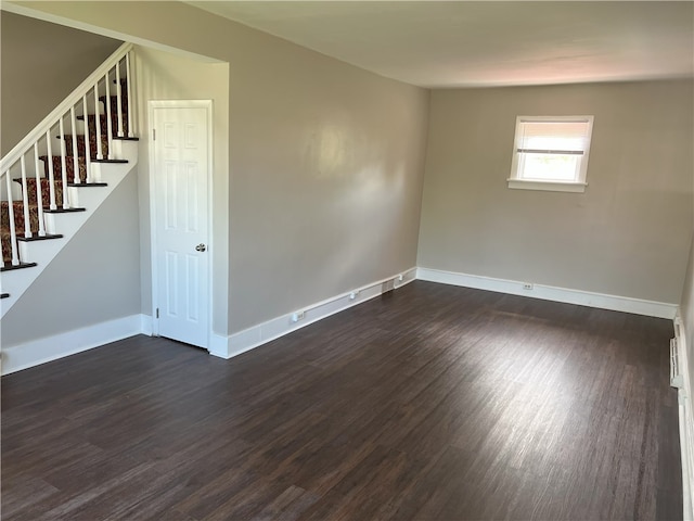 empty room with stairs, dark wood-type flooring, and baseboards