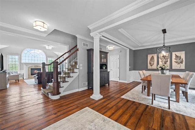 dining space with stairs, dark wood-style flooring, ornate columns, ornamental molding, and a fireplace