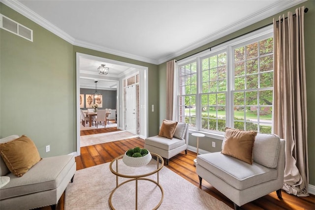 living area with wood-type flooring, ornamental molding, baseboards, and a chandelier