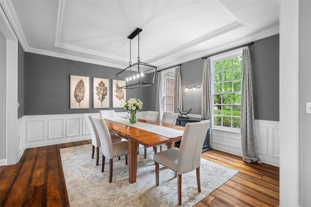 dining space featuring hardwood / wood-style floors, wainscoting, ornamental molding, a chandelier, and a decorative wall
