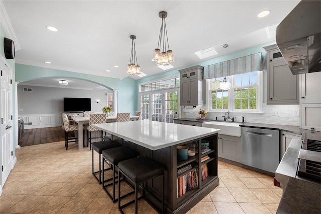 kitchen with stainless steel dishwasher, a sink, gray cabinetry, arched walkways, and a wainscoted wall