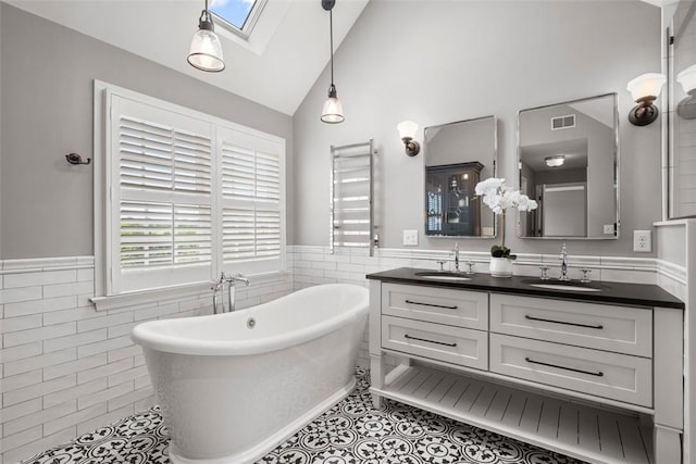 bathroom with a skylight, tile walls, tile patterned floors, a freestanding bath, and a wainscoted wall