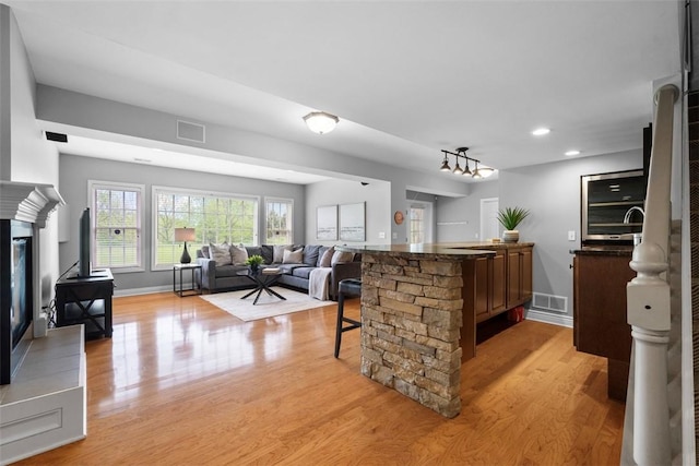 kitchen featuring light wood-style flooring, a breakfast bar, open floor plan, recessed lighting, and a glass covered fireplace