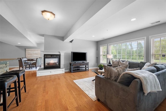living area featuring a multi sided fireplace, light wood finished floors, and baseboards