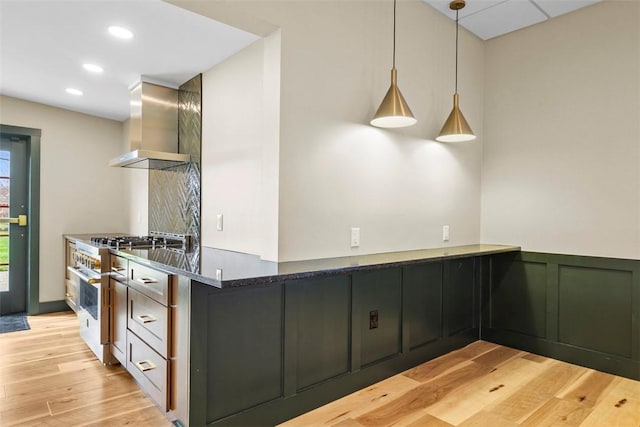 kitchen featuring wall chimney exhaust hood, light wood finished floors, hanging light fixtures, recessed lighting, and wainscoting