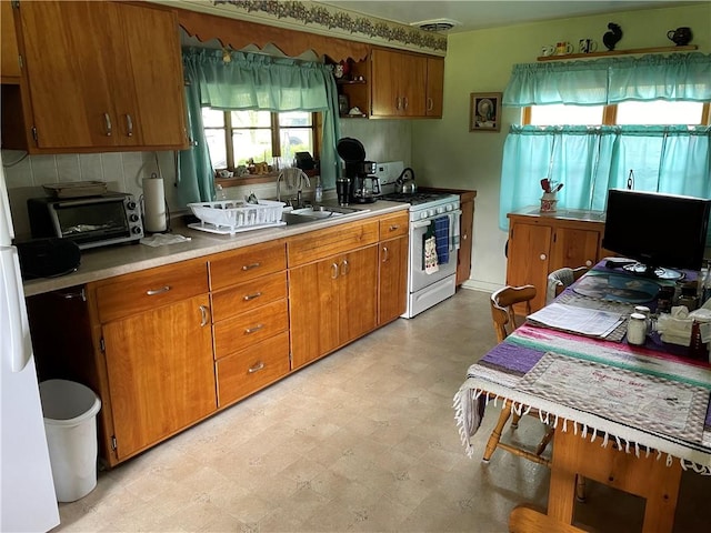 kitchen with white gas range, light flooring, brown cabinetry, light countertops, and decorative backsplash
