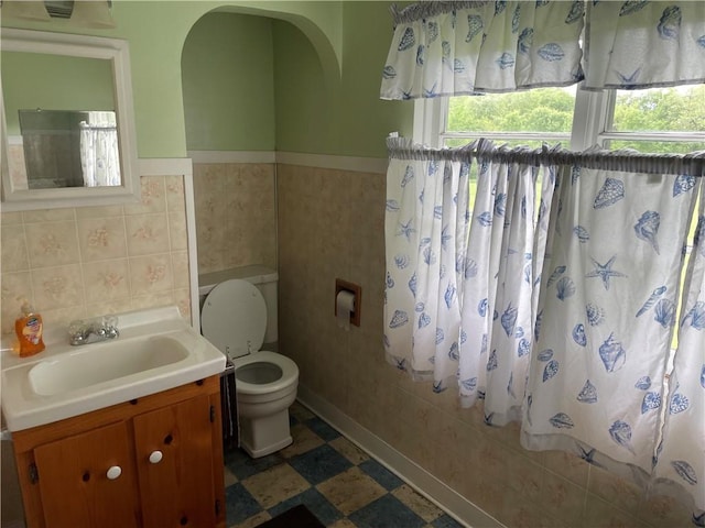 bathroom featuring toilet, tile patterned floors, wainscoting, tile walls, and vanity