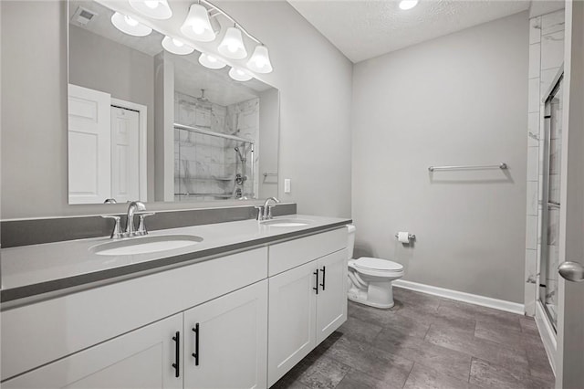 bathroom featuring a stall shower, baseboards, double vanity, toilet, and a textured ceiling