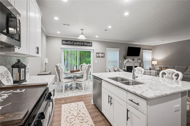 kitchen with appliances with stainless steel finishes, a sink, crown molding, open floor plan, and white cabinetry