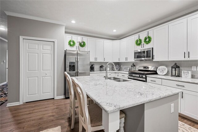kitchen with stainless steel appliances, a sink, a center island with sink, decorative backsplash, and ornamental molding