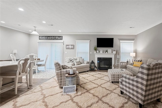 living area featuring healthy amount of natural light, wood finished floors, recessed lighting, ornamental molding, and a glass covered fireplace