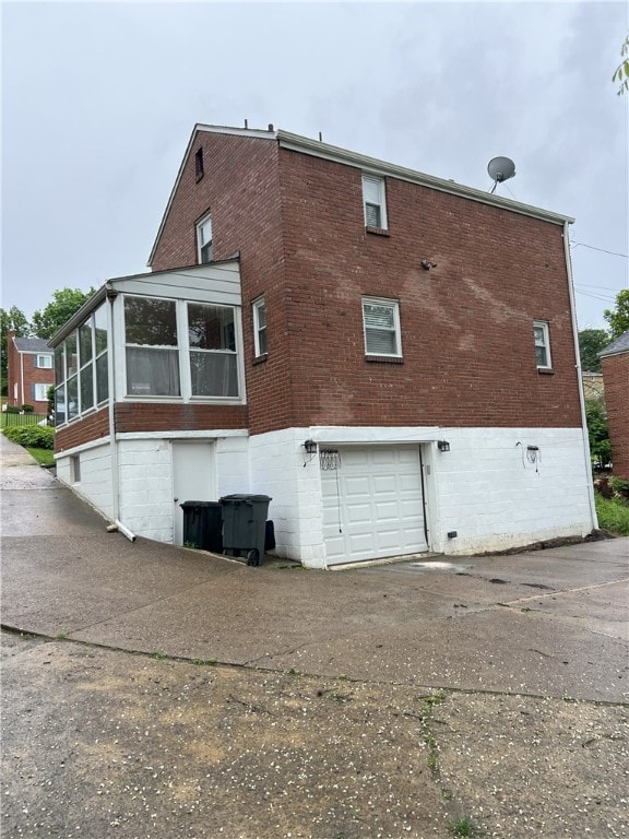 rear view of property featuring brick siding, a sunroom, a garage, and driveway