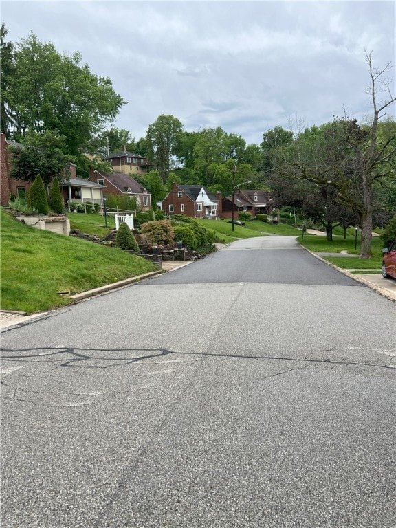view of asphalt street with a residential view, curbs, and street lights
