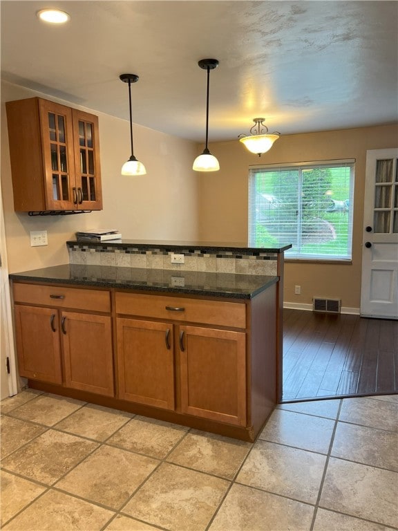 kitchen with a peninsula, brown cabinetry, glass insert cabinets, and dark stone counters