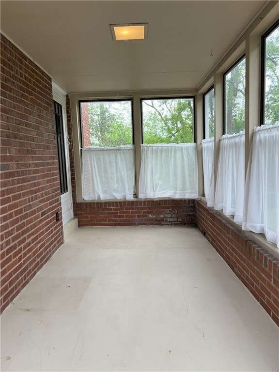 unfurnished sunroom featuring brick wall and concrete floors