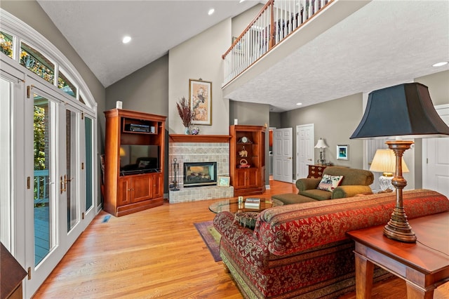 living area featuring light wood-type flooring, high vaulted ceiling, a glass covered fireplace, and recessed lighting