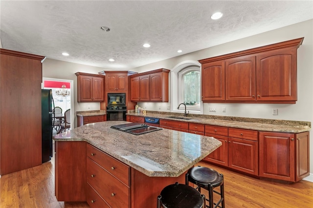 kitchen featuring black appliances, a sink, light wood-type flooring, a kitchen island, and recessed lighting